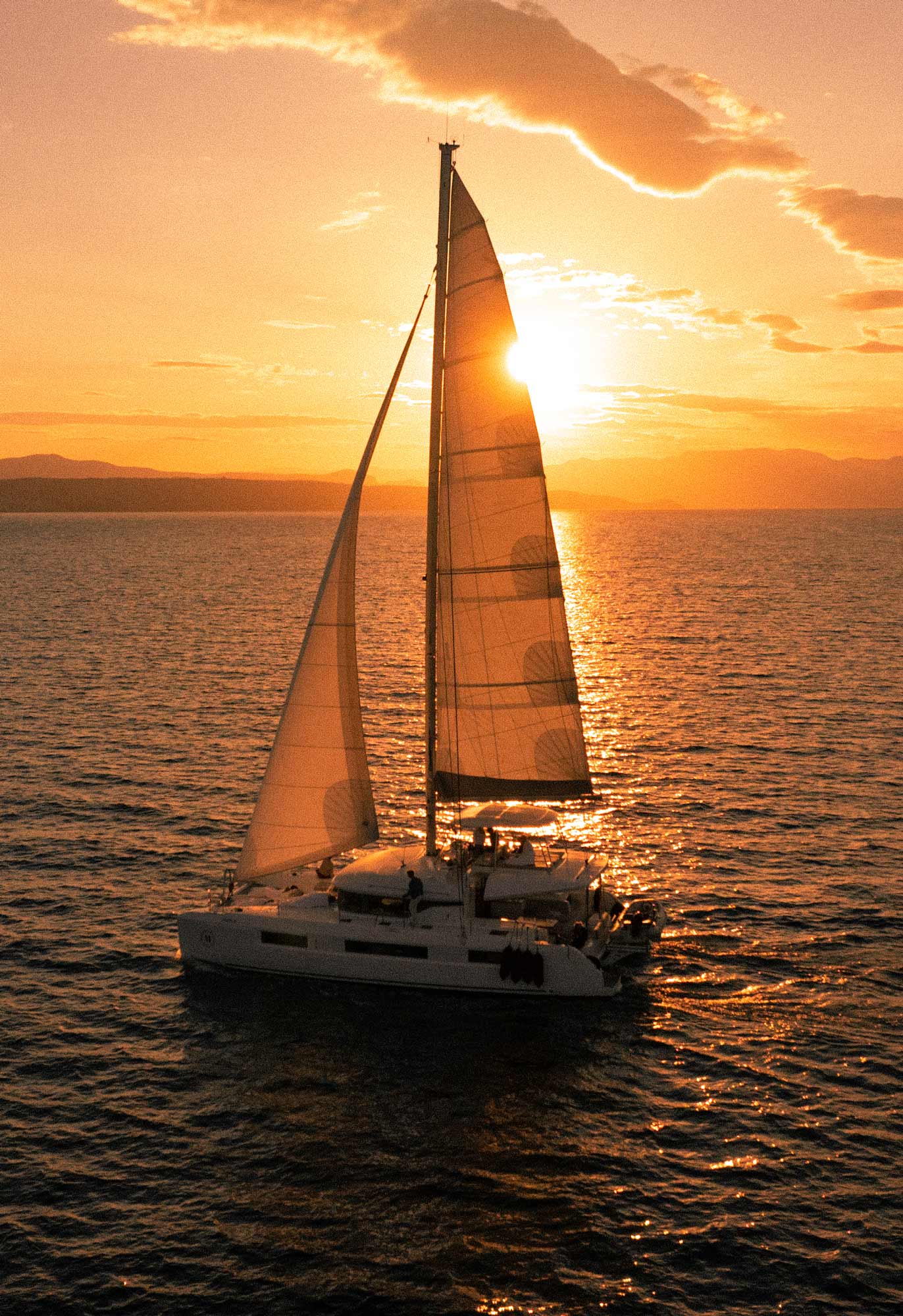A catamaran sails past at sunrise.